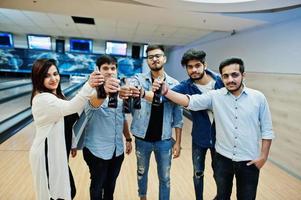 Group of five south asian peoples having rest and fun at bowling club. Clinking cold soda drinks from glass bottles. photo