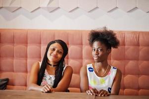 Two black african girlfriends at summer dresses sitting at table in cafe. photo