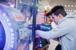 Two asian guys compete on shooter simulator game arcade machine. photo
