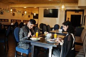 Encantadora pareja india enamorada, vestida con sari y traje elegante, sentada en el restaurante y comiendo postres juntos. foto