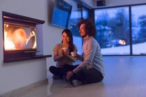 feliz pareja multiétnica sentada frente a la chimenea foto