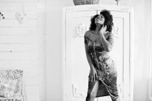 Afican american women in brilliant glitter sequins turqoise dress posed at white room against an old wardrobe. photo