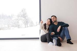 pareja multiétnica sentada en el suelo cerca de la ventana en casa foto