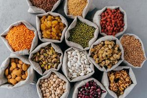 Dried food, harvest and protein from plant concept. Set of small hessian sacks filled with legumes, buckwheat, walnuts, banyan, chickpeas, muleberry and other. photo