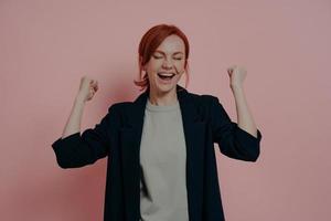 Young red-haired stylish woman screaming from excitement with closed eyes and clenched fists photo