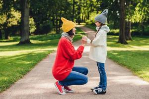 People, relationship, parenthood and childhood concept. Beautiful mother plays with her little daughter in park, gives yellow leaf, have sincere emotions and feeling or love to her lovely daughter photo