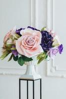 Vertical shot of artificial flowers on flower stand and tall vase against white background in spacious hall used as object of decoration. photo