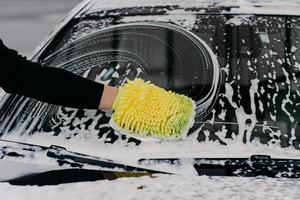 Car cleaning at self wash service. Mans hand with cloth washing cars windshied with foam soap. Auto cleaning concept. Selective focus photo