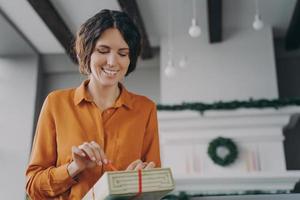 Attractive brunette Italian woman unpacking Christmas present gift box with red bow at home photo