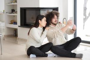 multiethnic couple using tablet computer in front of fireplace photo