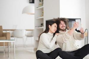 multiethnic couple using tablet computer in front of fireplace photo