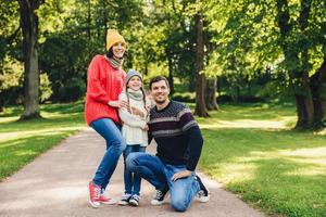 la familia tranquila y despreocupada ha caminado juntos, disfruta del clima soleado de otoño, el hermoso parque verde y el aire fresco, posan en la cámara, se abrazan, tienen una relación modelo. niño alegre y padres foto