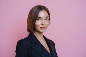 Isolated shot of pretty dark haired woman with healthy glowing skin, dressed formally, going to have formal meeting, wears makeup, poses against pink background. Successful businessewoman indoor photo