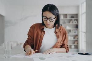 chica seria, empresaria está examinando informes. joven europea está trabajando a distancia desde casa. foto