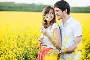 concepto de personas, relaciones, amor y libertad. pareja romántica pasa tiempo libre juntos en el campo de hermosas flores amarillas, se miran con gran amor, disfrutan de la unión y la calma foto