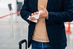 Keep your hands clean. Cropped shot of unrecognizable man disinfects hands with antibacterial napkin or antiseptic wet wipe during coronavirus spread, prevents virus, wants to be safe poses in airport photo