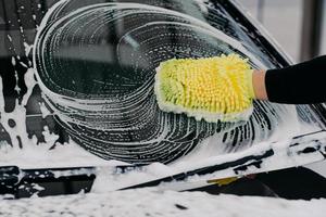 Car service concept. Unrecognizable man washes auto with cloth and car wash shampoo, has desire to cleanliness. Hand washing vehicle with sponge photo