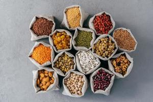 Raw healthy grain food and legume. Hessian bags of cereals and dried fruit. Packing groats at market against grey background photo