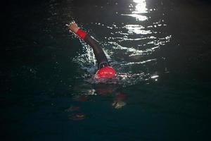 triathlon athlete swimming in dark night  wearing wetsuit photo