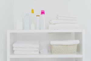 Laundry room with neatly folded towels, bottles of liquid washing or detergents. Everything in white colors. Daily chores and laundry day photo