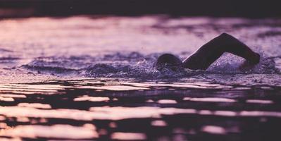 atleta de triatlón nadando en el lago al amanecer usando traje de neopreno foto