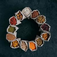 Photo of assorted legumes in hemp sacks standing around over dark background. Dried fruit, nuts and seeds. Agriculture concept