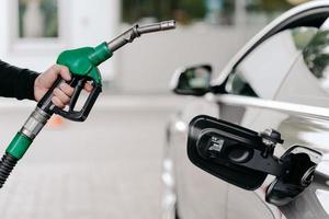 captura recortada de la mano del hombre bombeando combustible de gasolina en el coche en la gasolinera. auto siendo llenado con gasolina. el hombre irreconocible sostiene la boquilla de combustible. foto