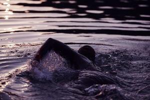 atleta de triatlón nadando en el lago al amanecer usando traje de neopreno foto