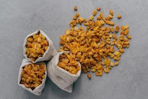 Burlap sacks with dry raisins spilled out over grey texture background. View from above. Dried fruit. Healthy nutrition concept photo