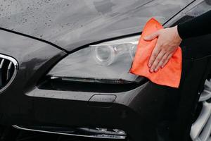 Mans hand wiping car headlight with microfiber cloth. Automobile detailing. Maintenance and transportation concept photo