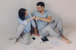 Positive female and male coworkers give fist bump to each other, work as team, calculate figures and prepare financial report, pose on floor, isolated over white background. Couple plan family budget photo