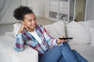 Teenage girl enjoying tv series watching and shifts channels. Afro young woman has morning leisure. photo