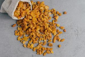 Image of sweet dried grapes spread from rustic sack, isolated over grey background. Yellow raisins containing useful vitamins photo