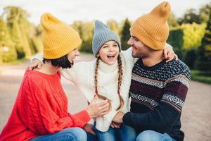 People, relationship and family concept. Smiling little girl with pigtails embrace her parents, express her positive emotions and feelings. Outdoor portrait of friendly family walk in beautiful park photo