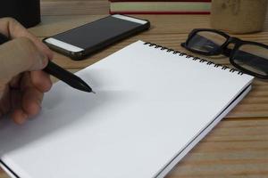 Hand with pen writing notebook on office desk table with. Copy space. photo