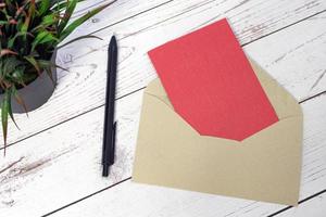 Red card mockup with envelope, pen and potted plant on wooden table. photo