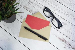 Red card mockup with envelope, pen, reading glasses and potted plant. Copy space photo