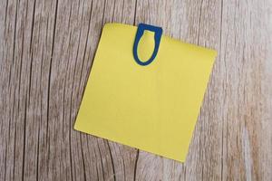 Yellow stick note on wooden table with blue paperclip. Directly above. photo