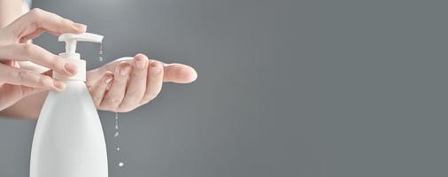 Female hands using hand sanitizer gel pump dispenser on gray background. Drops of gel close-up. Photo with copy space.