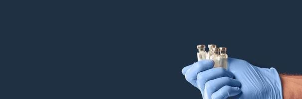 Blue gloved hand holding several vials isolated on dark background. photo