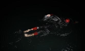 triathlon athlete swimming in dark night  wearing wetsuit photo