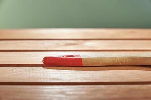 Freshly painted wood surface on a green background. The background is blurred. The wooden handle of the brush on the floor. photo