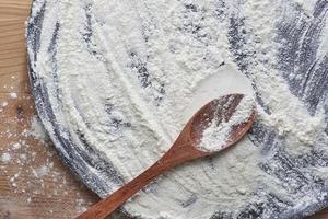 Overhead shot of used wooden chopping board and wooden spoon scattered with white flour. photo