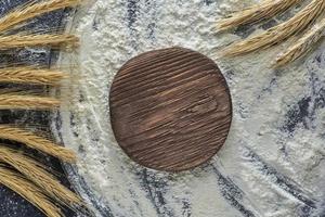 Wheat ear, wheat flour and cutting board on wooden background, top view. Photo with copy space.