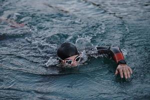 triathlon athlete swimming on lake in sunrise  wearing wetsuit photo