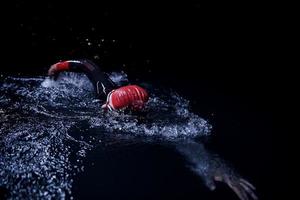 atleta de triatlón nadando en la noche oscura con traje de neopreno foto