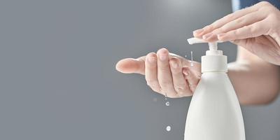 Female hands using hand sanitizer gel pump dispenser on gray background. Drops of gel close-up. Photo with copy space.