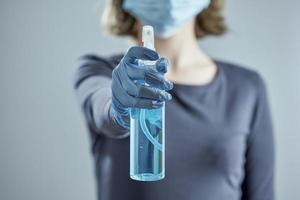 A girl in a medical mask and rubber gloves in blur holds out sanitizer.
