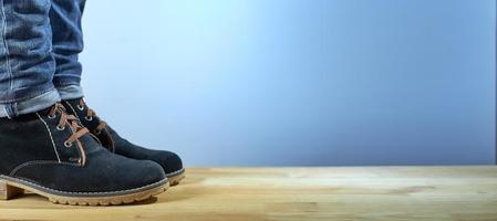 Female legs in demi-season boots and blue jeans on wooden floor on a blue background. Fashion background. Photo with copy space.