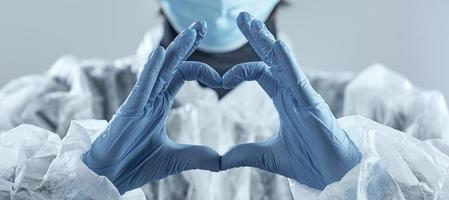 Woman in medical mask and hands in latex glove shows the symbol of the heart. photo